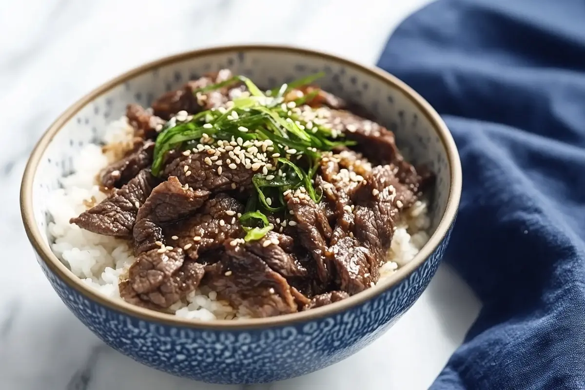 A bowl of thinly sliced beef over rice, garnished with chopped green onions and sesame seeds.